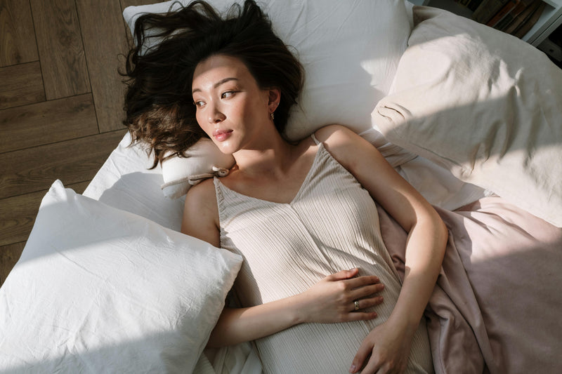 Alt: A pregnant woman touching her belly while lying on a bed.