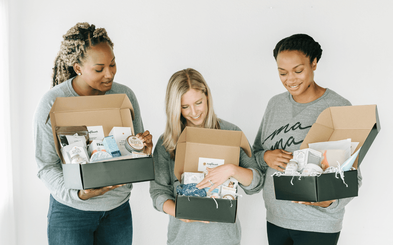 Three women posing with boxes in front of a white wall.