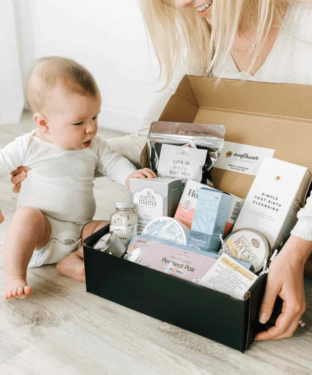 A woman holding a baby in a box filled with diverse products, showcasing the range of items available.