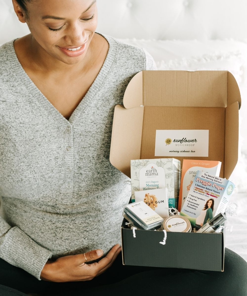 A pregnant woman smiling while holding a box of baby products.