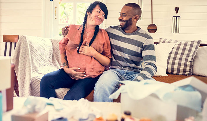 A man and a pregnant woman looking at baby clothes together.