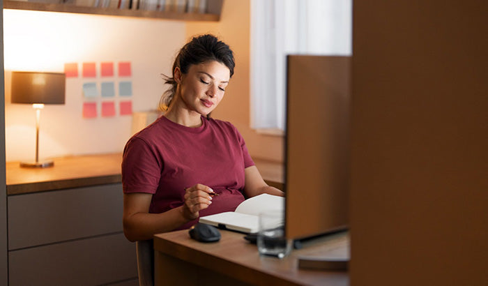 A pregnant woman at her desk, balancing work with her laptop and pen, embodying the challenges of work-life balance.