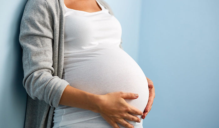 A pregnant woman stands against a wall, showcasing a thoughtful mom-to-be care package for her pregnancy journey.