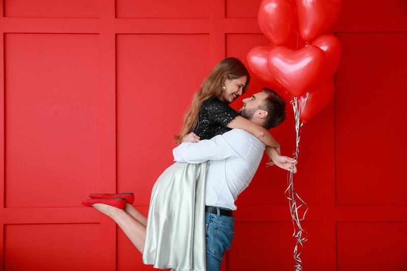 A cheerful couple holds red heart-shaped balloons, radiating joy