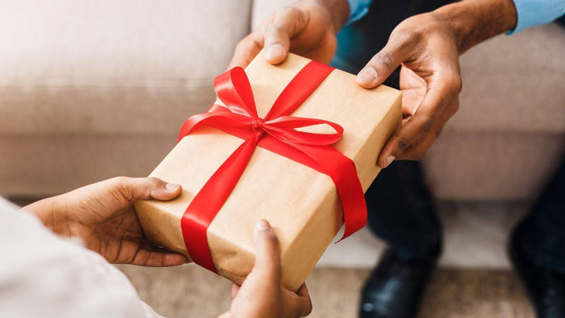 A man gives a wrapped gift to another, highlighting their friendship