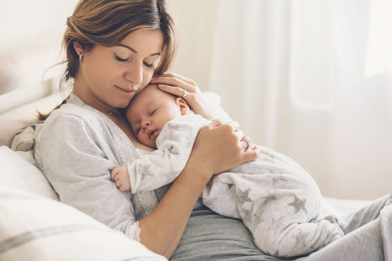 A mother tenderly holding her sleeping baby on a bed.