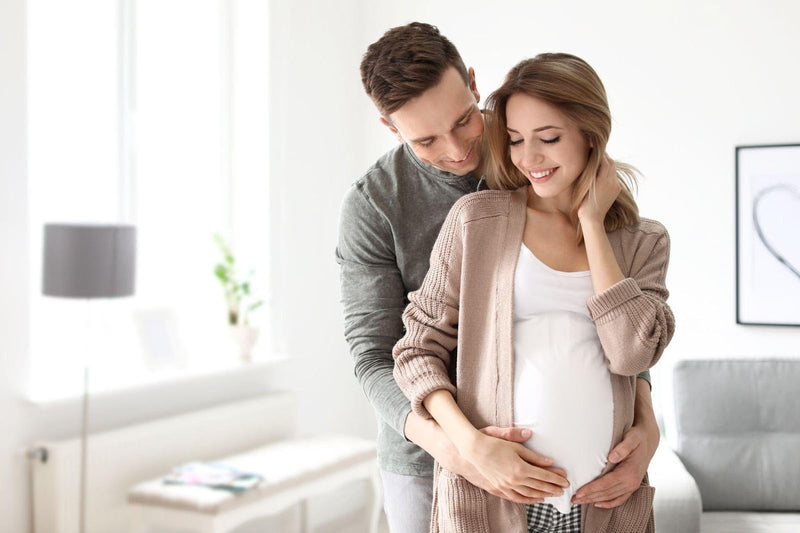 A Pregnant Woman And A Man Stand In A Cozy Warmly Lit Living Room