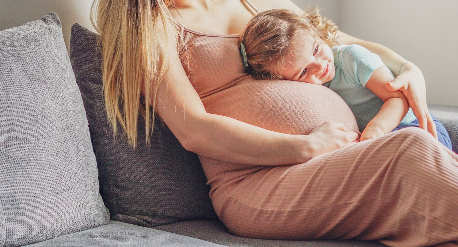 A pregnant woman cuddling a young child on a couch.