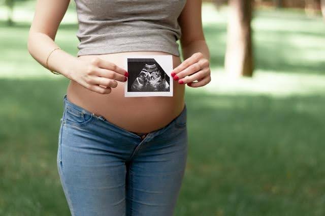A pregnant woman smiles while holding a photo of her baby showcasing her joy and anticipation for motherhood