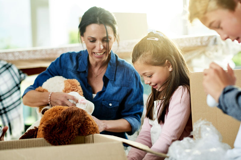 A smiling mother and daughter unpacking stuffed animals from cardboard boxes during a move.