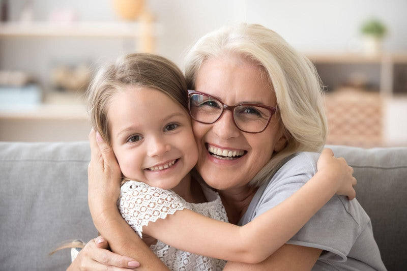 A woman and a young girl embrace affectionately while sitting together on a cozy couch