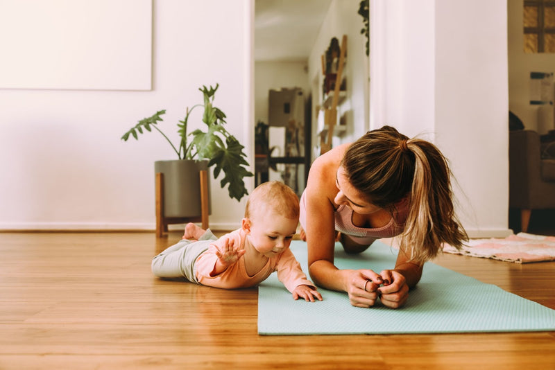 A woman and her baby practice yoga together on a mat, demonstrating a peaceful and nurturing exercise environment.