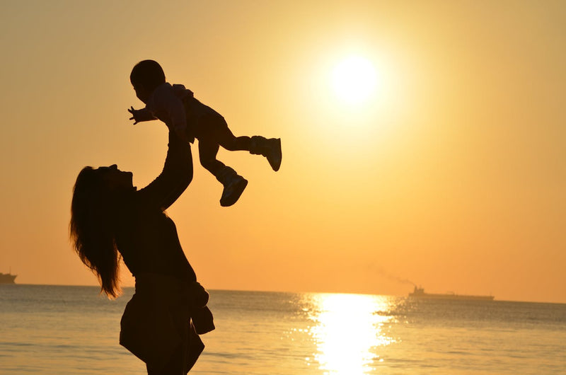 Alt: Silhouette of a mother with a baby on a beach during sunset.