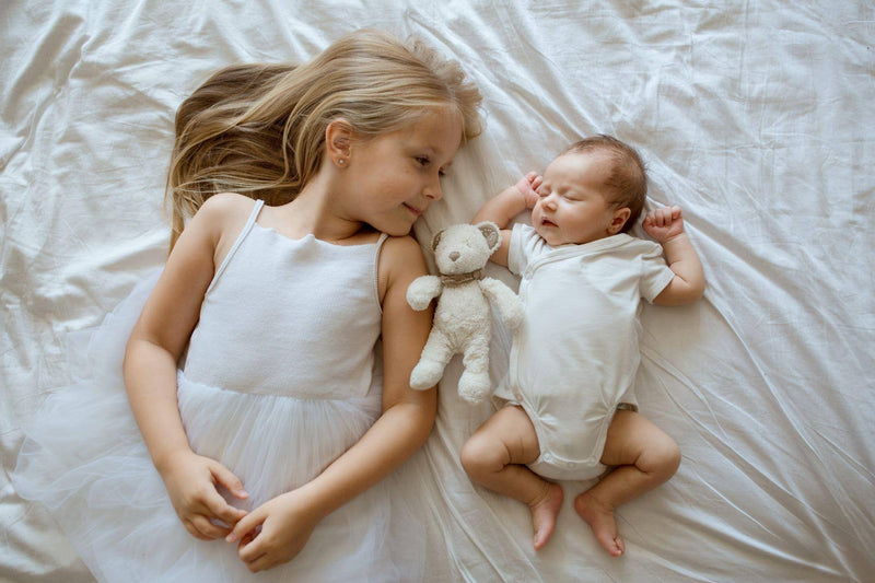 Two little girls dressed in white dresses playfully lying on a bed radiating joy and friendship