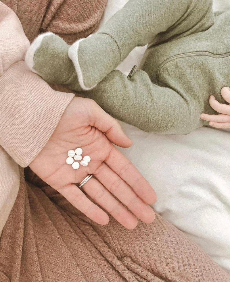 mom holding a pill while her baby's lying on the bed