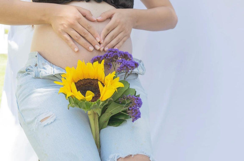 pregnant woman shaping heart on her hands with lavender and sunflower