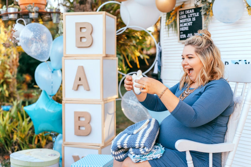 Pregnant woman with baby shower decorations including balloons and wooden blocks spelling 'BABY'.