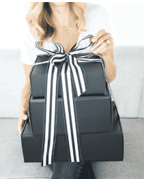 A woman holding a black and white gift box, looking excited and smiling.