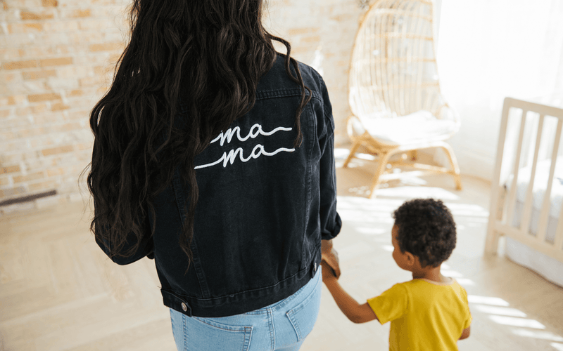 A woman in a denim jacket with the word "mama" on it, smiling brightly.